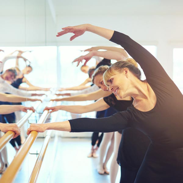 adult ballet class at the barre working on a combra while stretching