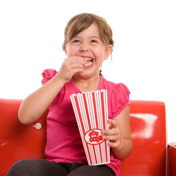 young girl smiling and eating popcorn while watching a movie