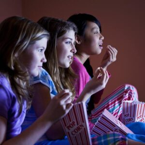 three teenagers watching a movie and eating popcorn