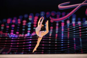 Young lyrical soloist doing a firebird jump on stage at competition